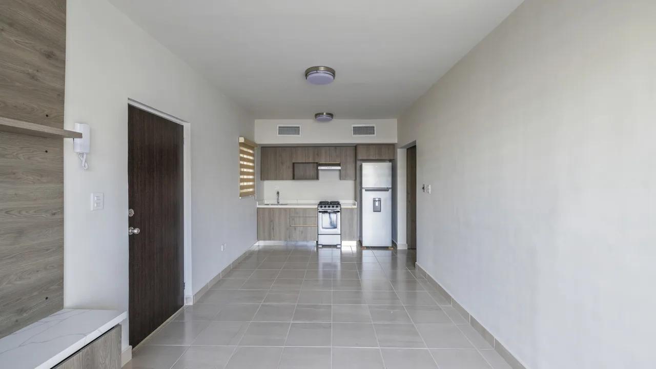 Sala del departamento muestra sin amueblar, con ventanal y luz natural